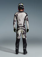 Zawodnik motocrossowy w kompletnym zestawie Alpinestars 2026 Racer Lahnd, widok z tyłu, bluza i spodnie Sand Camo z jasnoszarym i czarnym abstrakcyjnym wzorem, czarny kask, czarno-neonowożółte rękawice, czarne buty, logo „astars” na tyle spodni