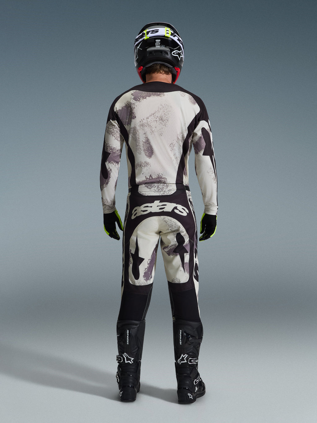 Motocyklista motocrossowy widziany od tyłu w koszulce 2026 Racer Lahnd i pasujących spodniach w kolorze Sand Camo, z kremowo-szarym abstrakcyjnym wzorem i czarnymi panelami, brandingiem „astars” na spodniach, czarnymi butami Alpinestars i czarnym kaskiem, kompletny off-roadowy wygląd wyścigowy.