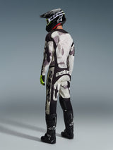 Spodnie Alpinestars 2026 Racer Lahnd w kolorze Sand Camo i szarym, pełny zestaw odzieży motocrossowej z pasującą bluzą, czarnym kaskiem i butami, widok z tyłu prezentujący wyrazisty branding i ergonomiczną konstrukcję
