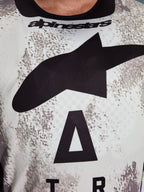 Alpinestars 2026 Racer Lahnd Jersey, koszulka motocrossowa, biało-szary nakrapiany wzór, zbliżenie na klatkę piersiową z dużym czarnym logo Astars i brandingiem Alpinestars na dekolcie, konstrukcja zorientowana na wydajność do jazdy off-road