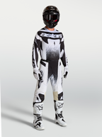 Spodnie Alpinestars Techstar Swan, męskie spodnie motocrossowe, czarne i białe, sportowy krój wyścigowy, elastyczny materiał ripstop, model w pełnym zestawie odzieży wyścigowej z kaskiem i butami.