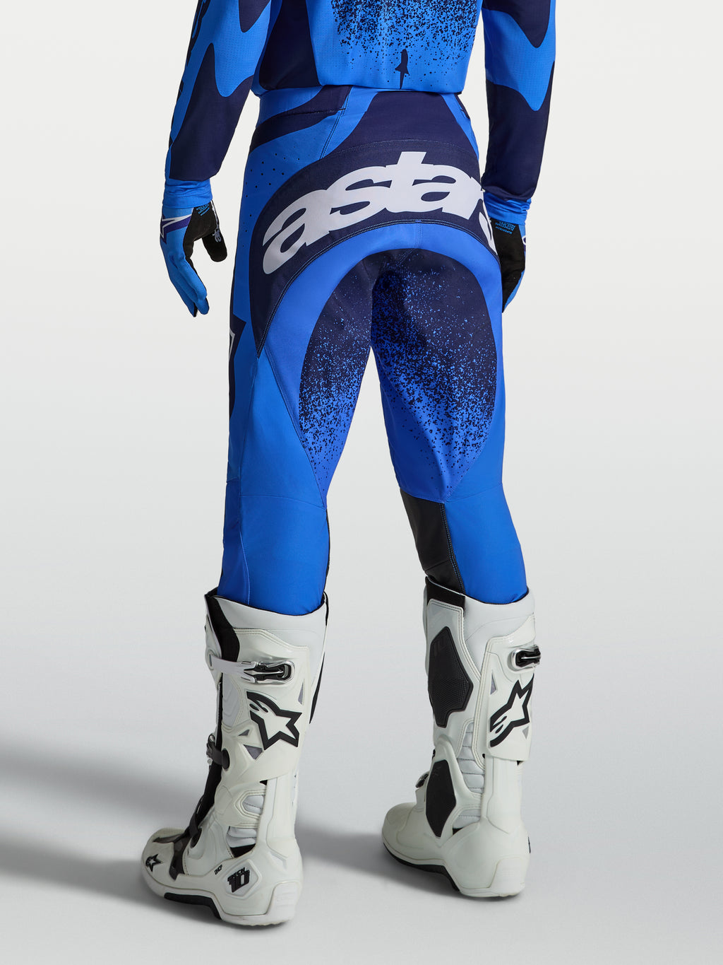 Spodnie Techstar Swan marki Alpinestars, męskie spodnie motocrossowe, niebieskie i ciemnoniebieskie, widok z tyłu z dużym białym logo na siedzisku, profesjonalna odzież do jazdy terenowej.