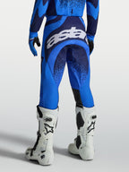 Spodnie Techstar Swan marki Alpinestars, męskie spodnie motocrossowe, niebieskie i ciemnoniebieskie, widok z tyłu z dużym białym logo na siedzisku, profesjonalna odzież do jazdy terenowej.