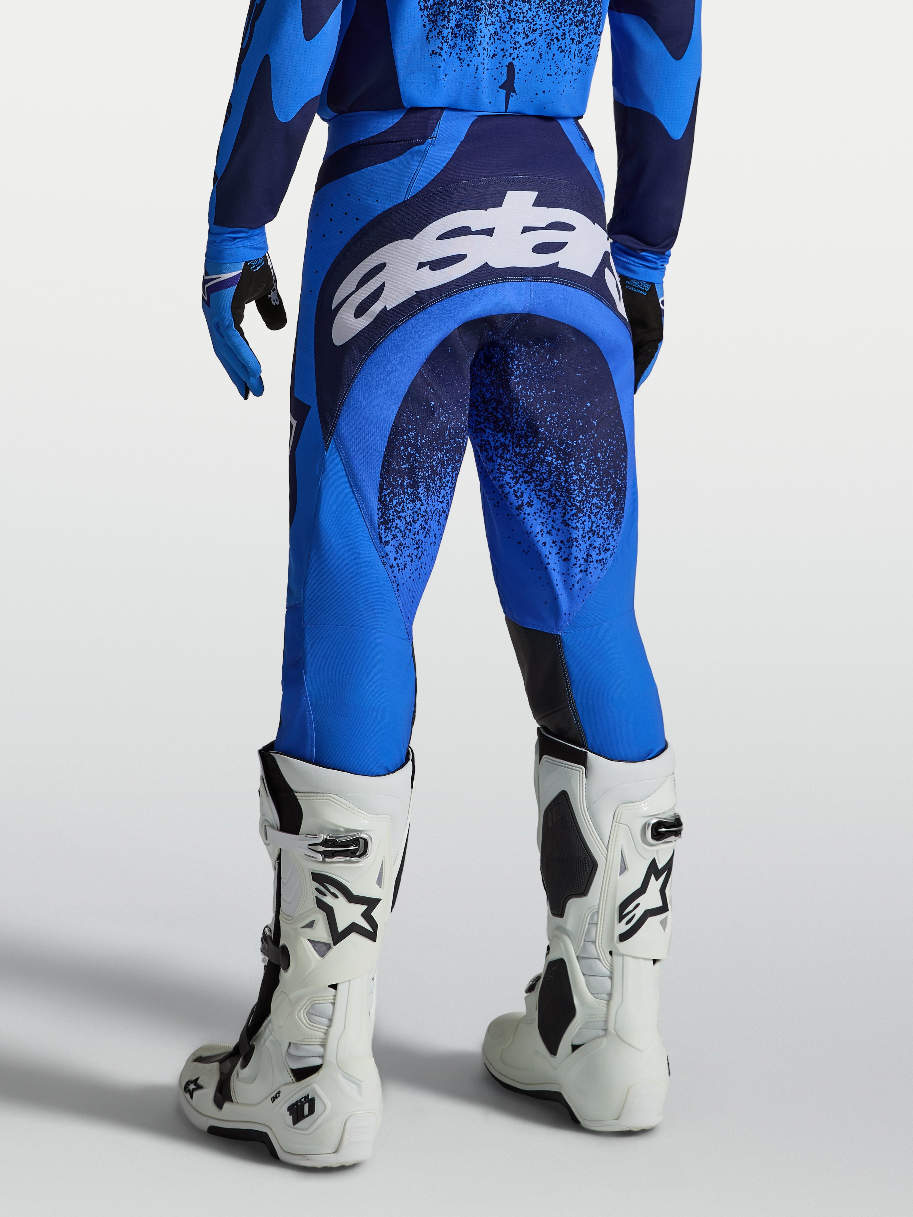 Spodnie Techstar Swan marki Alpinestars, męskie spodnie motocrossowe, niebieskie i ciemnoniebieskie, widok z tyłu z dużym białym logo na siedzisku, profesjonalna odzież do jazdy terenowej.