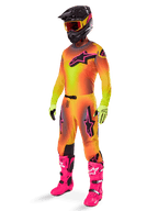 Alpinestars Supertech Lipan Pants 2025, spodnie motocrossowe, żółto-różowe, noszone jako część pełnego zestawu z dopasowaną koszulką z gradientem, jaskraworóżowymi butami, żółtymi rękawicami i czarnym kaskiem, z wyraźnymi czarnymi logotypami i sportowym krojem do wyścigów off-road