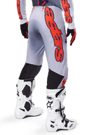 Spodnie Alpinestars Supertech Lipan 2025, spodnie motocrossowe, szare i pomarańczowe fluo, widok z tyłu z dużą pomarańczową grafiką Alpinestars, czarne elastyczne panele, zestaw z pasującą koszulką i białymi butami, profesjonalna odzież wyścigowa