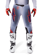 Spodnie Alpinestars Supertech Lipan 2025, spodnie motocrossowe, szaro-pomarańczowe fluo, zestawione z czerwono-czarnymi rękawicami i biało-czarnymi butami, z dużymi logotypami gwiazdy Alpinestars na udach oraz perforacjami wentylacyjnymi dla profesjonalnych zawodników.