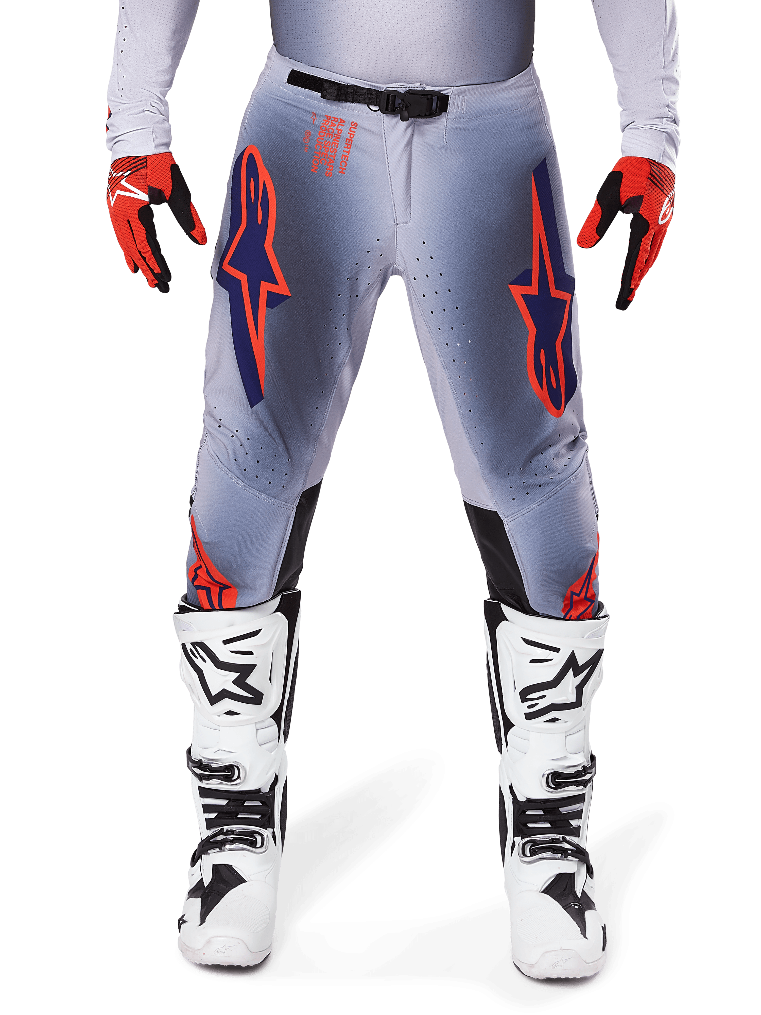 Spodnie Alpinestars Supertech Lipan 2025, spodnie motocrossowe, szaro-pomarańczowe fluo, zestawione z czerwono-czarnymi rękawicami i biało-czarnymi butami, z dużymi logotypami gwiazdy Alpinestars na udach oraz perforacjami wentylacyjnymi dla profesjonalnych zawodników.