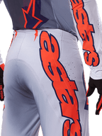 Alpinestars 2025 Supertech Lipan Pants and Jersey, zestaw odzieży motocrossowej, szary i pomarańczowy fluo, zbliżenie na bok i tył z dużym pomarańczowym logo Alpinestars, techniczny materiał rip-stop z perforowaną wentylacją
