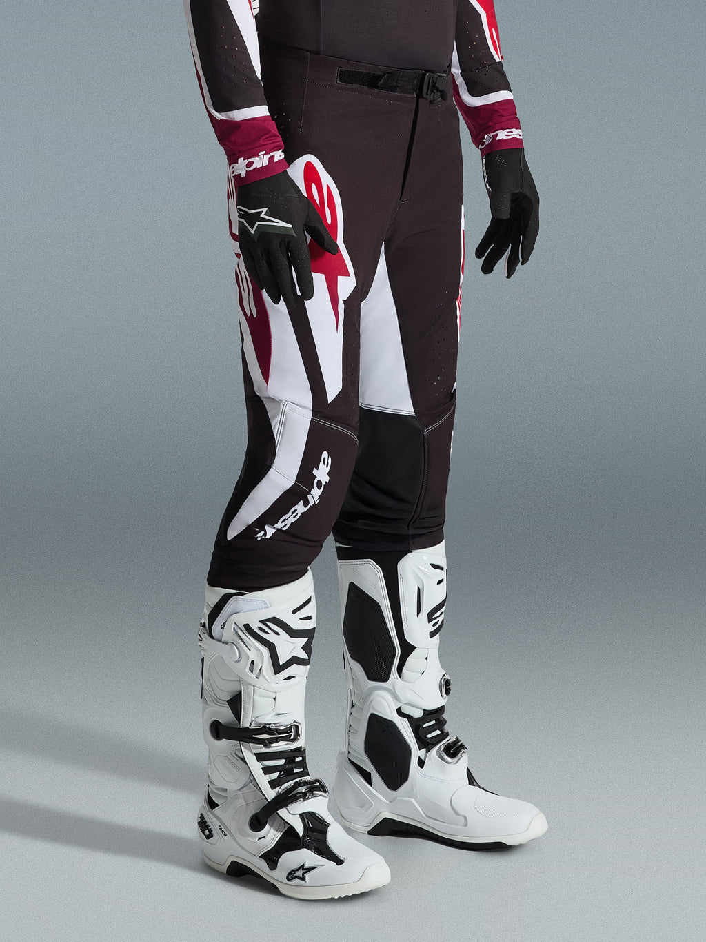 Alpinestars 2026 Supertech AFD Vista Pants, spodnie motocrossowe, czarno-czerwono-białe, noszone z biało-czarnymi butami motocrossowymi i czarnymi rękawicami, duże białe i czerwone wzory graficzne, atletyczny krój wyścigowy