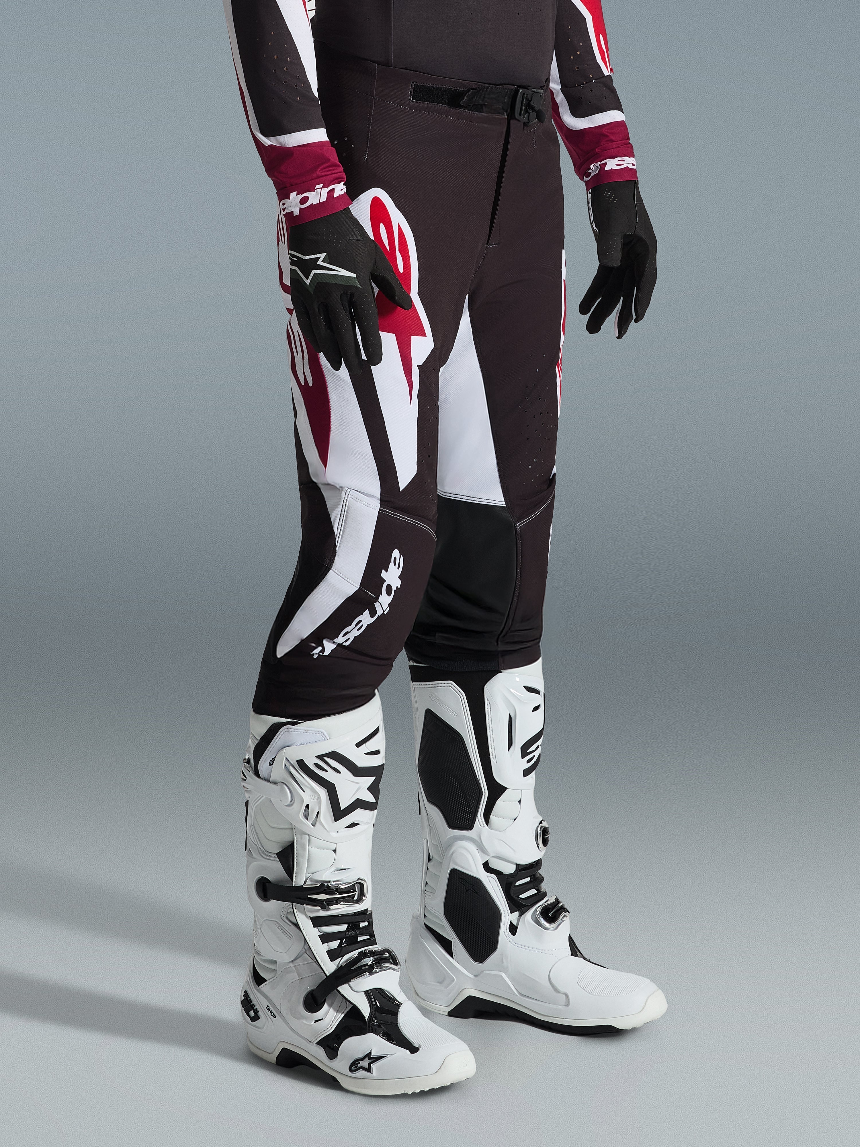 Alpinestars 2026 Supertech AFD Vista Pants, spodnie motocrossowe, czarno-czerwono-białe, noszone z biało-czarnymi butami motocrossowymi i czarnymi rękawicami, duże białe i czerwone wzory graficzne, atletyczny krój wyścigowy