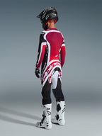 Zawodnik motocrossowy od tyłu w spodniach Alpinestars 2026 Supertech AFD Vista, czarno-czerwono-białe, dopasowana koszulka, czarny kask i biało-czarne buty, widok od tyłu na całą sylwetkę w profesjonalnym stroju wyścigowym