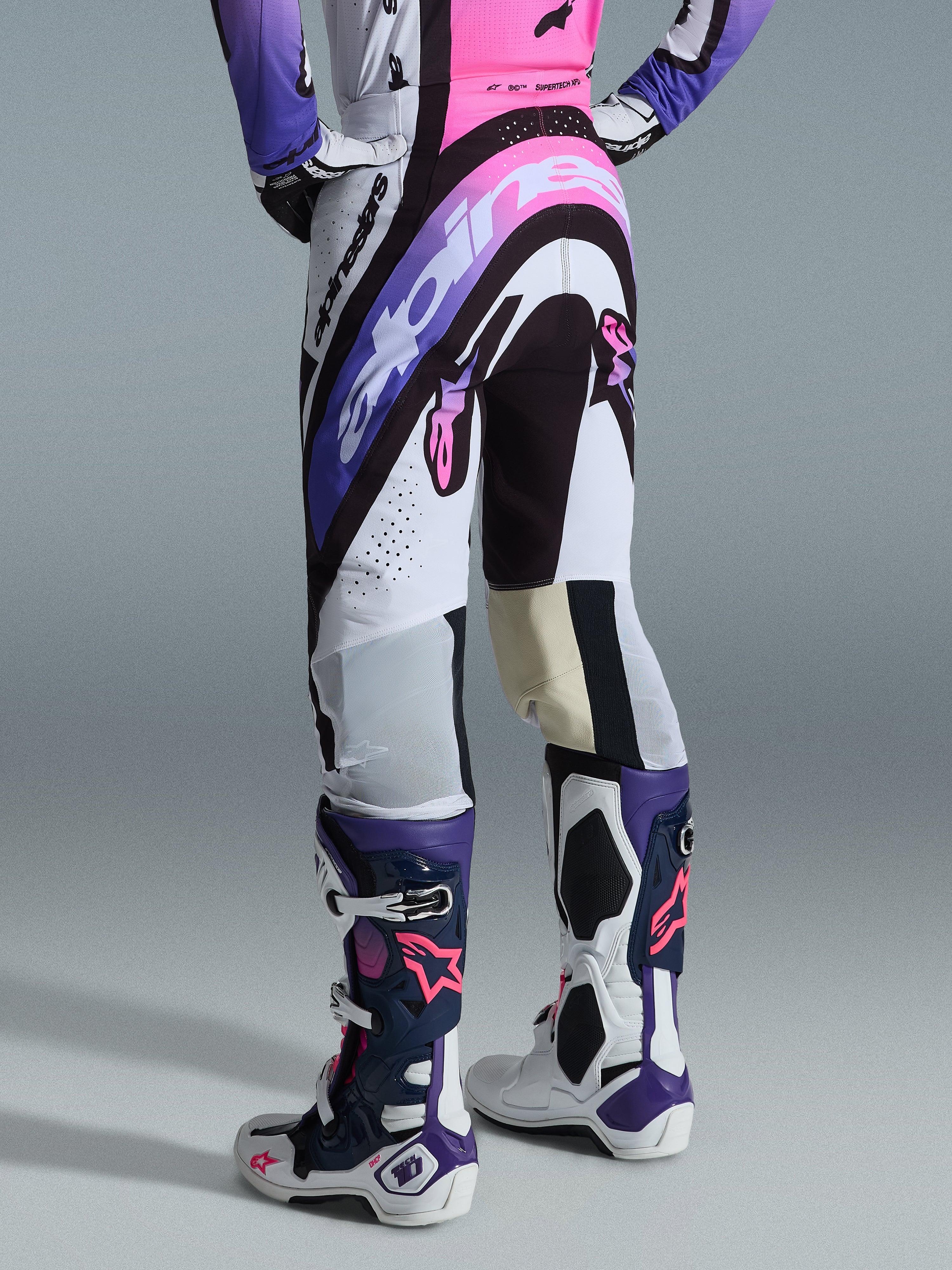 Alpinestars Supertech AFD Vista Pants 2026, spodnie motocrossowe, białe, fioletowe i czarne z różowymi akcentami, widok z tyłu w zestawie z pasującą koszulką i butami Tech 10, wyraziste grafiki logo i materiały techniczne do profesjonalnych wyścigów terenowych