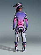 Zawodnik motocrossowy widziany od tyłu w pełnym stroju wyścigowym, koszulka z fioletowo-różowym gradientem, spodnie Alpinestars 2026 Supertech AFD Vista w kolorze biało-fioletowo-czarnym, czarny kask z fioletowymi goglami, biało-fioletowe buty, skoordynowany zestaw wyścigowy off-road
