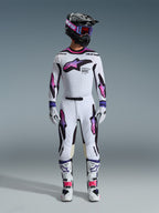 Motocyklista motocrossowy w kompletnym zestawie wyścigowym, spodnie i koszulka Alpinestars 2026 Supertech AFD Vista w kolorach białym, fioletowym i czarnym, dopasowane rękawice, biało-czarne buty, czarny kask z fioletowymi goglami, sportowy krój zapewniający wydajność w terenie