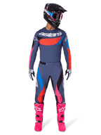 Alpinestars Techstar Dreem Pants 2025, spodnie motocrossowe, szare wielokolorowe z różowymi i niebieskimi akcentami, noszone przez motocyklistę w dopasowanej koszulce technicznej, czarnym kasku i jaskraworóżowych butach, kompletny profesjonalny zestaw wyścigowy off-road