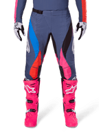Alpinestars 2025 Techstar Dreem Pants, spodnie motocrossowe, szary wielokolorowy z różowymi, niebieskimi i pomarańczowymi akcentami, noszone z jaskraworóżowymi butami motocrossowymi i pasującą koszulką, sportowy krój wyścigowy z laserowo wycinanymi otworami wentylacyjnymi