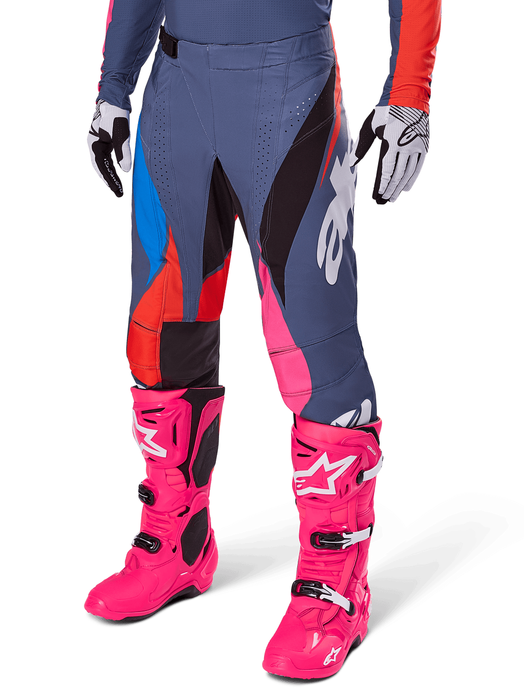 Alpinestars Techstar Dreem Pants 2025, spodnie motocrossowe, ciemnoszare z niebieskimi, czerwonymi i różowymi panelami, białe grafiki, noszone z jaskraworóżowymi butami i czarno-białymi rękawicami, wyrazisty design o wysokiej widoczności