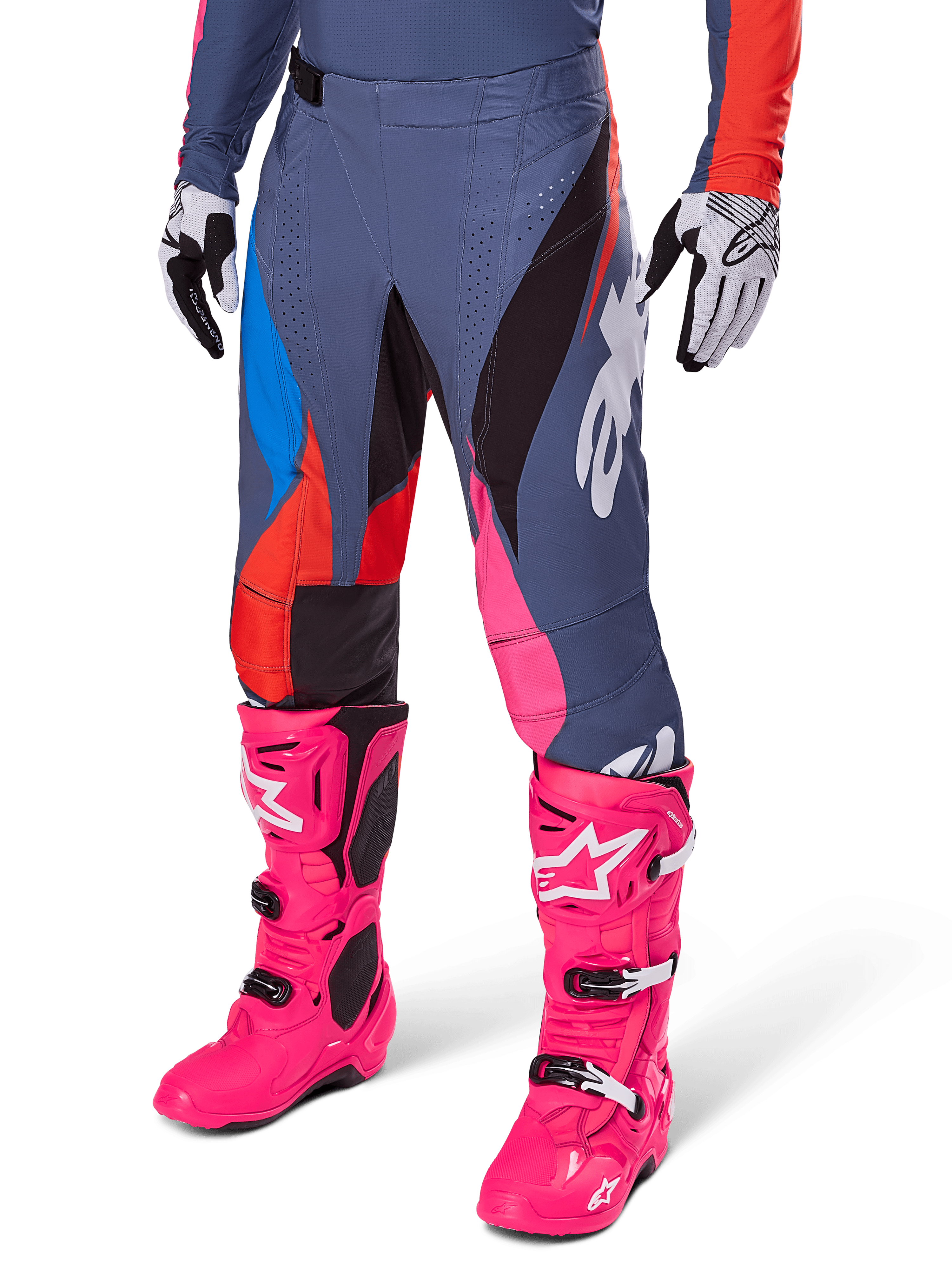 Alpinestars Techstar Dreem Pants 2025, spodnie motocrossowe, ciemnoszare z niebieskimi, czerwonymi i różowymi panelami, białe grafiki, noszone z jaskraworóżowymi butami i czarno-białymi rękawicami, wyrazisty design o wysokiej widoczności