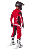 Alpinestars 2025 Techstar Dreem Pants, spodnie motocrossowe, jaskrawoczerwone i czarne, widziane z tyłu na motocykliście w pełnym stroju wyścigowym z dopasowaną czerwoną koszulką, czarnym kaskiem i białymi butami, wyraźne białe logo Alpinestars i czarne elastyczne panele.