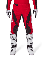Alpinestars Techstar Dreem Pants 2025, spodnie motocrossowe, jaskrawoczerwone i czarne, z kanciastymi wzorami i laserowo wycinanymi otworami wentylacyjnymi, noszone z białymi butami motocrossowymi i pasującymi rękawicami do wyścigów terenowych