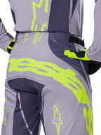 Spodnie Alpinestars Techstar Dreem 2025, spodnie motocrossowe, szare i ciemnoszare z neonowymi żółtymi akcentami, widok z tyłu prezentujący wyraźne logo Alpinestars na karczku, noszone z pasującą koszulką i rękawicami, zaprojektowane do wyścigów terenowych