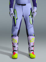 Alpinestars 2026 Supertech Scenz Pants, spodnie motocrossowe, fioletowo-żółte fluo, z dużymi neonowo-żółtymi logo na udach, zestawione z pasującymi fioletowo-żółtymi butami i rękawicami motocrossowymi, sportowy krój wyczynowy do wyścigów terenowych
