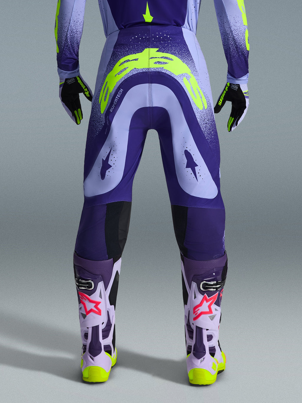 Alpinestars 2026 Supertech Scenz Pants, spodnie motocrossowe, fioletowe i neonowożółte (fluo), widok z tyłu pokazujący duże żółte logo na siedzeniu, w zestawie z pasującą bluzą, rękawicami i butami ochronnymi, sportowy krój do profesjonalnych wyścigów motocrossowych