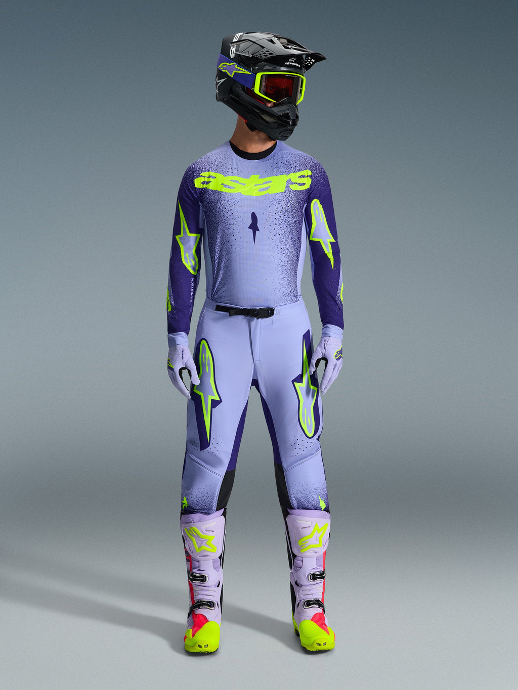 Spodnie Alpinestars Supertech Scenz 2026, spodnie motocrossowe, fioletowe i żółte fluo, noszone jako kompletny zestaw wyścigowy z pasującą lawendową bluzą, rękawicami i butami, z wyrazistymi żółtymi neonowymi logotypami, sportowy krój do profesjonalnych wyścigów terenowych