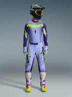 Spodnie Alpinestars Supertech Scenz 2026, spodnie motocrossowe, fioletowe i żółte fluo, noszone jako kompletny zestaw wyścigowy z pasującą lawendową bluzą, rękawicami i butami, z wyrazistymi żółtymi neonowymi logotypami, sportowy krój do profesjonalnych wyścigów terenowych