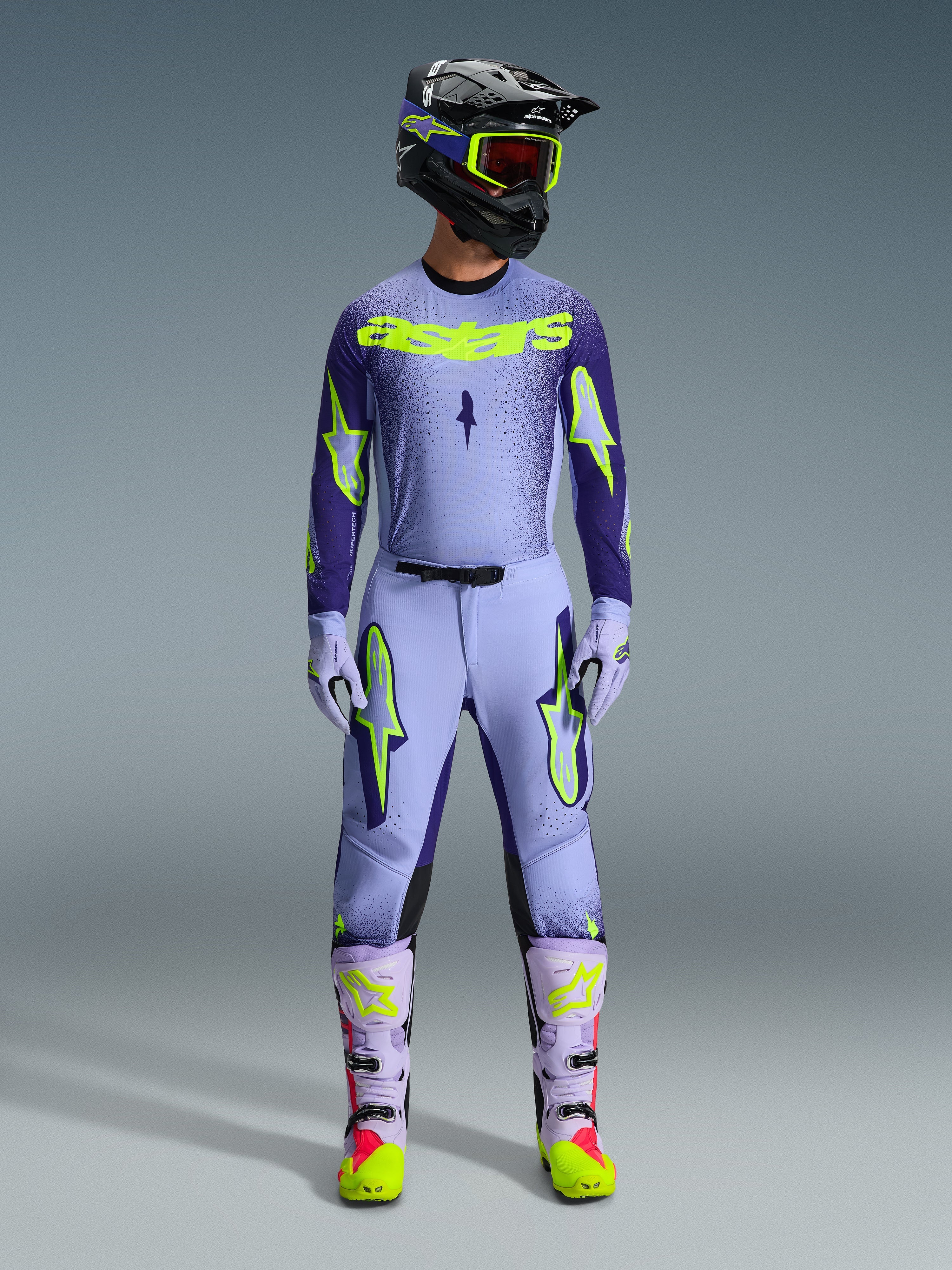 Spodnie Alpinestars Supertech Scenz 2026, spodnie motocrossowe, fioletowe i żółte fluo, noszone jako kompletny zestaw wyścigowy z pasującą lawendową bluzą, rękawicami i butami, z wyrazistymi żółtymi neonowymi logotypami, sportowy krój do profesjonalnych wyścigów terenowych