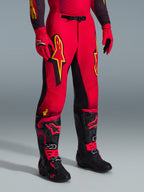 Alpinestars 2026 Supertech Scenz Pants, spodnie motocrossowe, czerwone, czarne i żółte, z żółtymi logotypami Alpinestars i czarnymi panelami, noszone z pasującą czerwoną koszulką, czerwonymi rękawicami i czarnymi butami motocrossowymi.