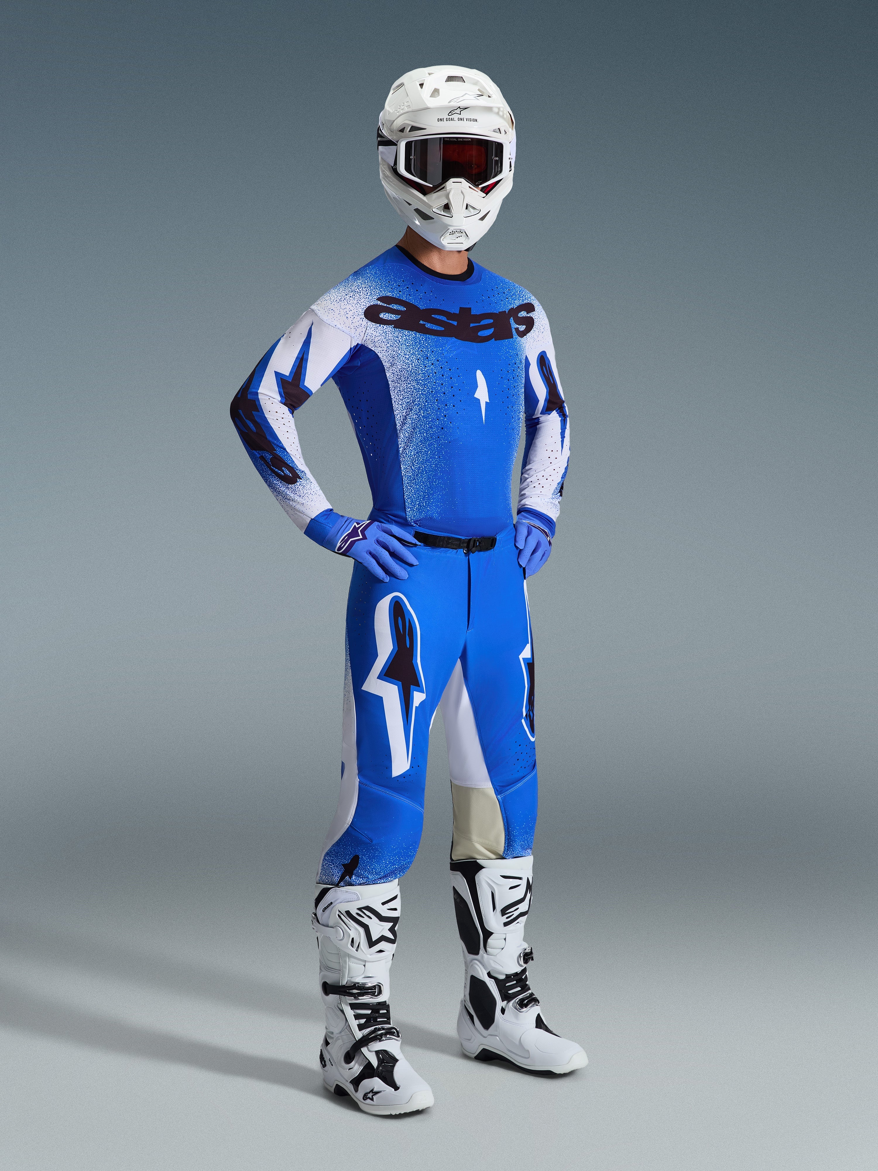 Zawodnik motocrossowy w pełnym stroju wyścigowym, spodnie 2026 Supertech Scenz w kolorze Ucla Blue i białym, dopasowana niebiesko-biała koszulka z logo Astars, biały kask z czerwonymi goglami, biało-czarne buty, profesjonalny zestaw do wyścigów off-road