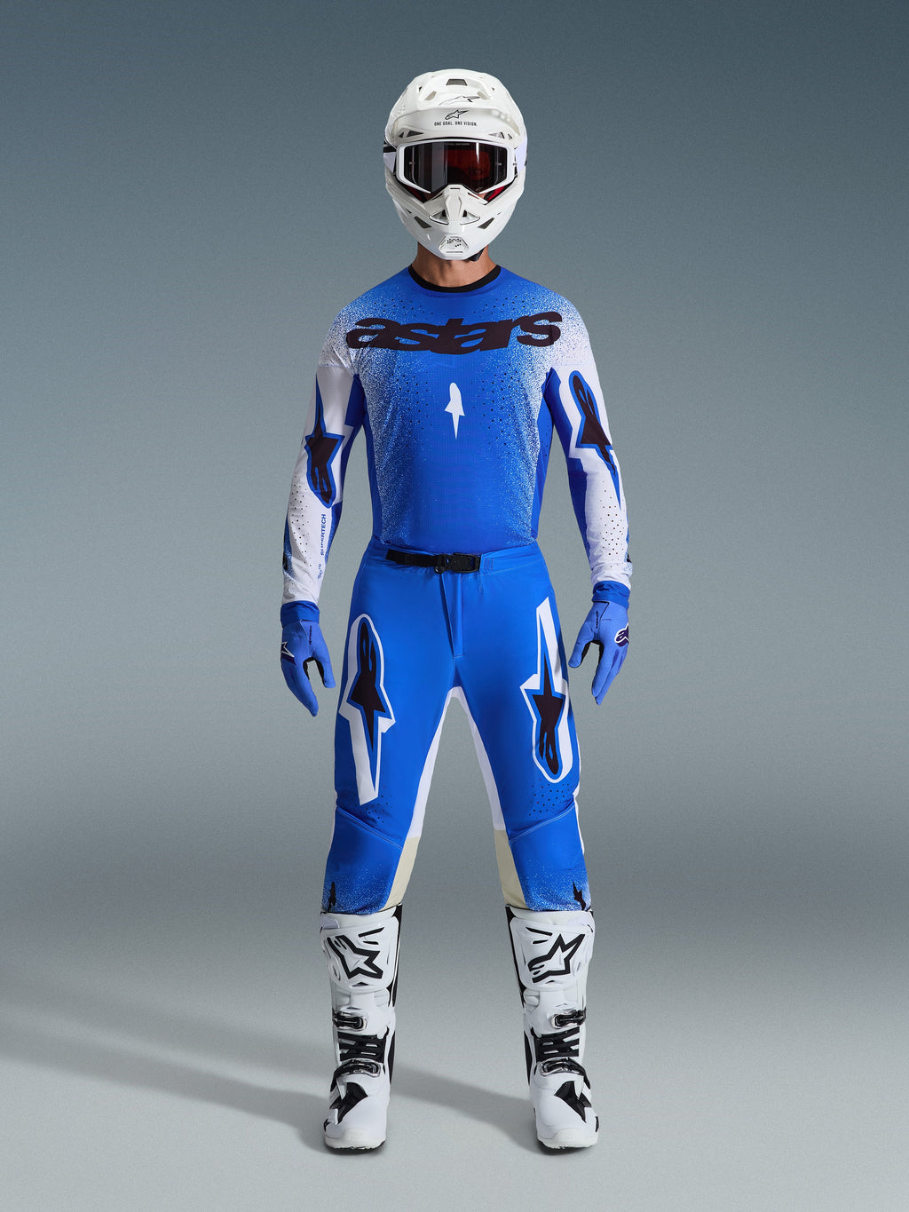 Zawodnik motocrossowy w pełnym stroju wyścigowym, niebiesko-biała koszulka z czarnym brandingiem astars, spodnie 2026 Supertech Scenz w kolorze Ucla Blue White z wyraźnymi logotypami gwiazdy, biały kask, niebieskie rękawice i białe buty, skoordynowany sportowy strój wyścigowy