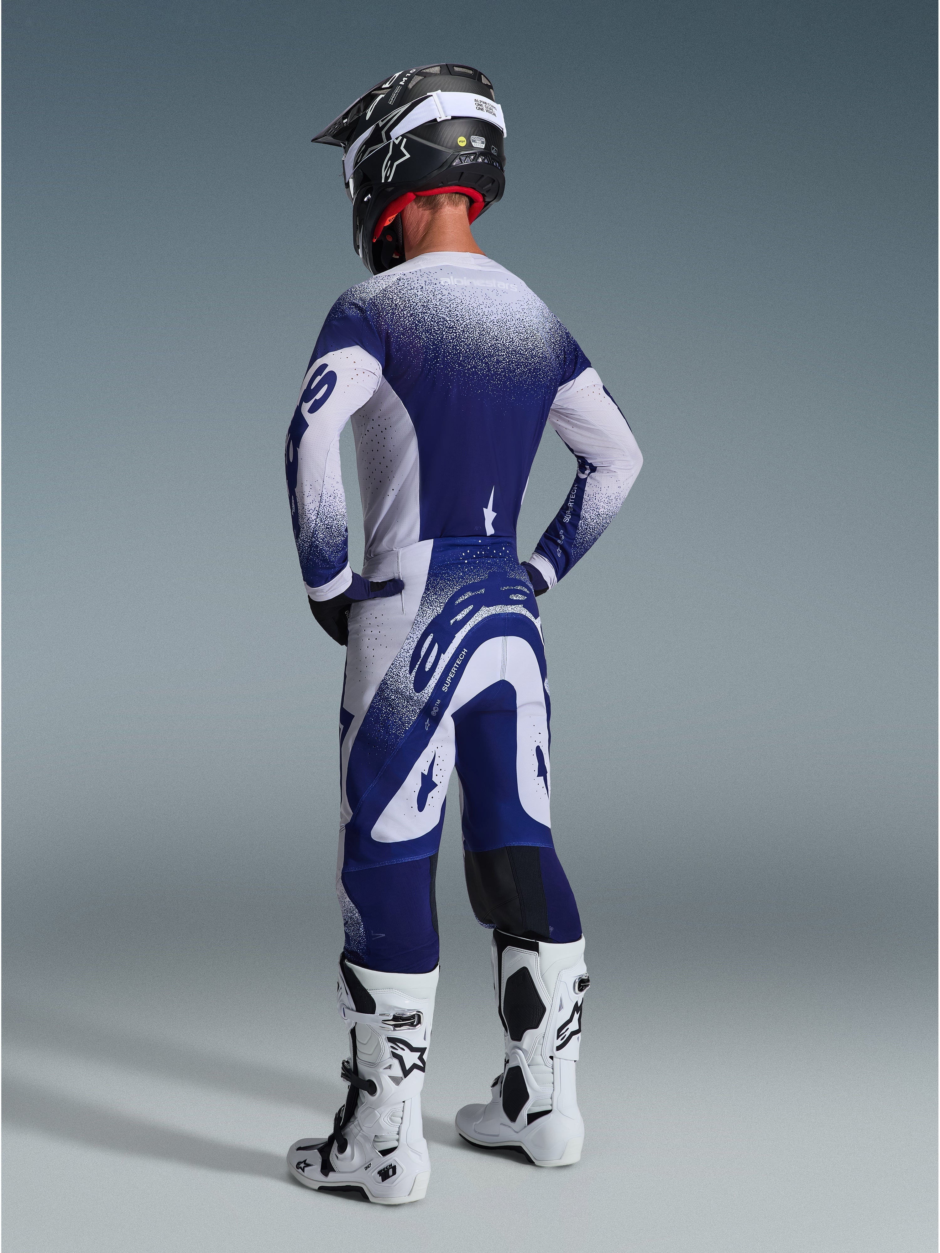 Alpinestars Supertech Scenz Pants 2026, spodnie motocrossowe, jasnoszare i ciemnoniebieskie, widok z tyłu w zestawie z pasującą koszulką i białymi butami, grafika z gradientowymi kropkami, sportowy krój wyczynowy do wyścigów off-road.