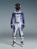 Motocyklista motocrossowy ubrany w zestaw Alpinestars Supertech Scenz 2026, biało-granatowa koszulka i pasujące spodnie z dużym logo Astars i nakrapianym wzorem graficznym, czarny kask, biało-czarne buty ochronne oraz dopasowane niebieskie rękawice, kompletny profesjonalny strój wyścigowy