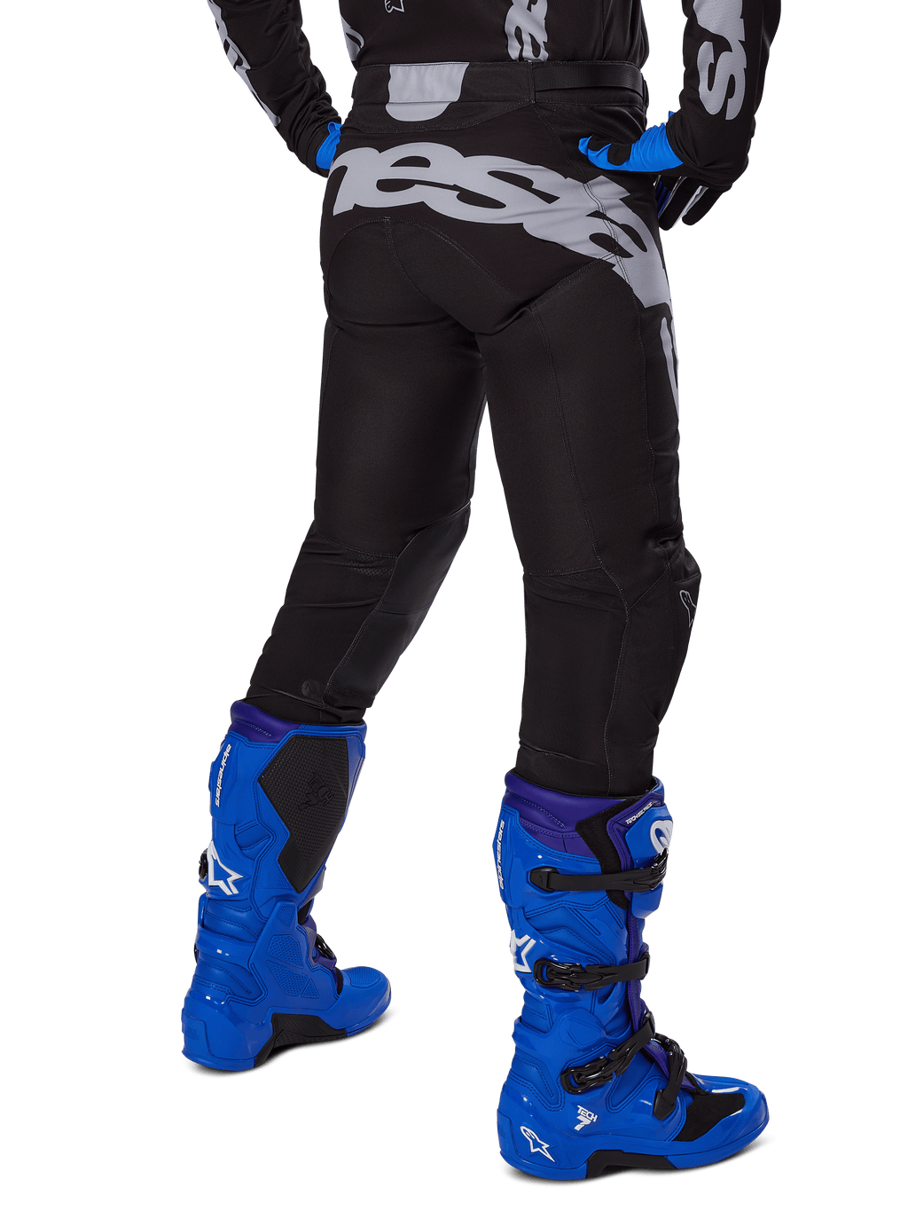 Alpinestars 2025 Racer Graphite Pants, spodnie motocrossowe, czarno-szare, widok z tyłu z dużym szarym brandingiem na siedzeniu, zestawione z jaskrawoniebieskimi butami motocrossowymi i czarno-niebieską koszulką, wytrzymała odzież off-road