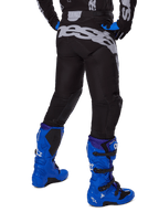 Alpinestars 2025 Racer Graphite Pants, spodnie motocrossowe, czarno-szare, widok z tyłu z dużym szarym brandingiem na siedzeniu, zestawione z jaskrawoniebieskimi butami motocrossowymi i czarno-niebieską koszulką, wytrzymała odzież off-road