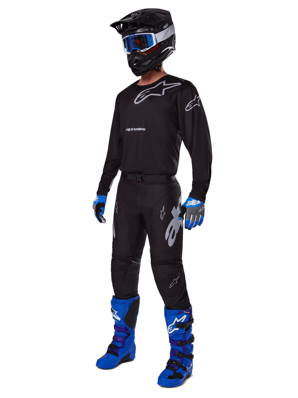 Motocyklista motocrossowy w kompletnym stroju wyścigowym Alpinestars, spodnie Racer Graphite 2025 w kolorze czarno-szarym, pasująca czarna bluza z szarym logo, czarny kask z niebieskimi goglami, jaskrawoniebieskie i fioletowe buty oraz niebiesko-szare rękawice, dopasowany strój do wyścigów terenowych