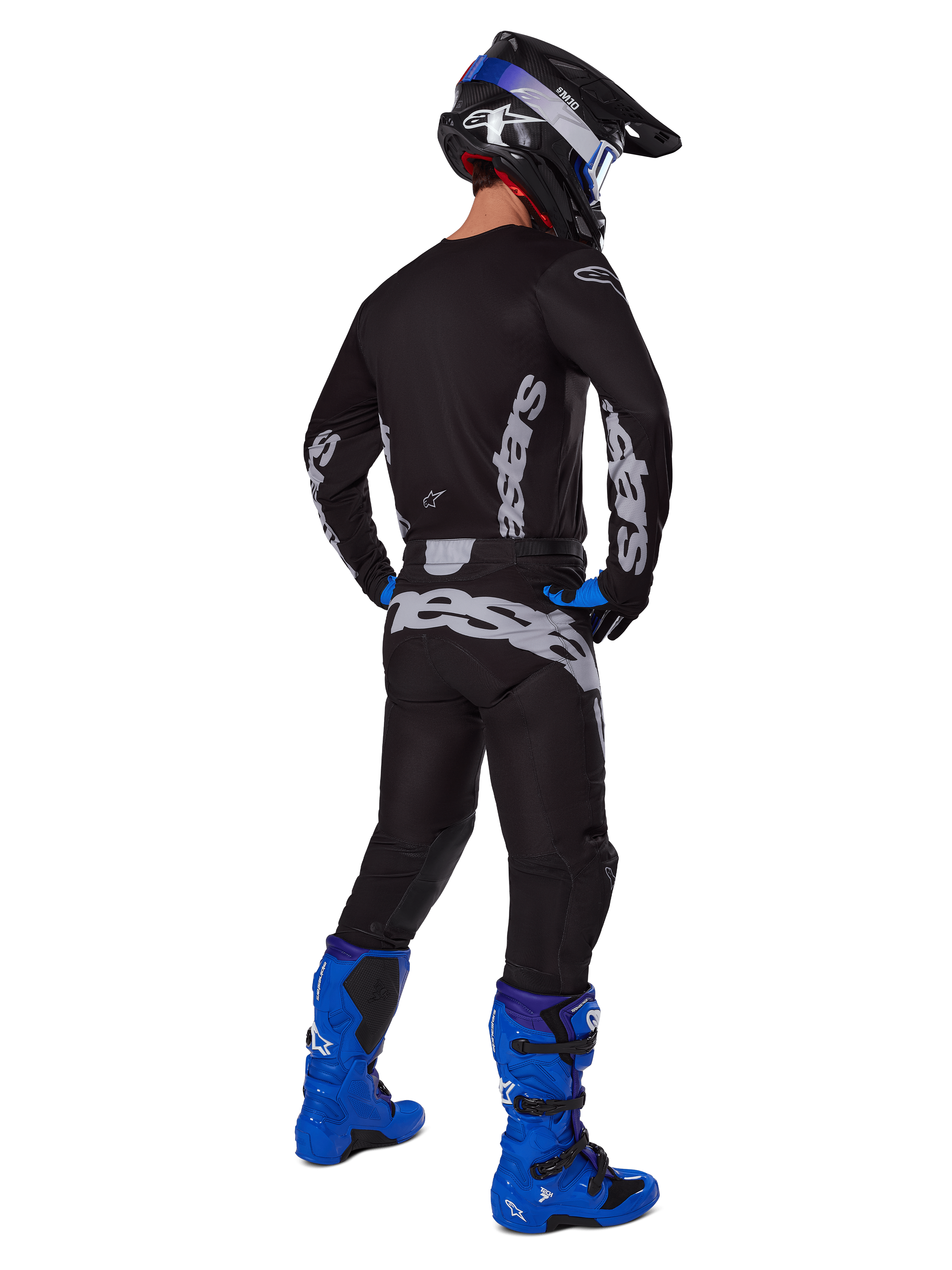 Alpinestars 2025 Racer Graphite Pants, spodnie motocrossowe, czarno-szare, widok od tyłu zawodnika w pełnym stroju z dopasowaną bluzą i jaskrawoniebieskimi butami, duże szare logo na siedzeniu, ergonomiczny, wstępnie zakrzywiony krój do jazdy terenowej