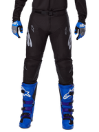 Alpinestars 2025 Racer Graphite Pants, spodnie motocrossowe, czarno-szare, noszone z niebiesko-szarymi rękawicami i niebieskimi butami, srebrny branding Astars na udach i wzmocnione kolana, sportowy design do jazdy w terenie