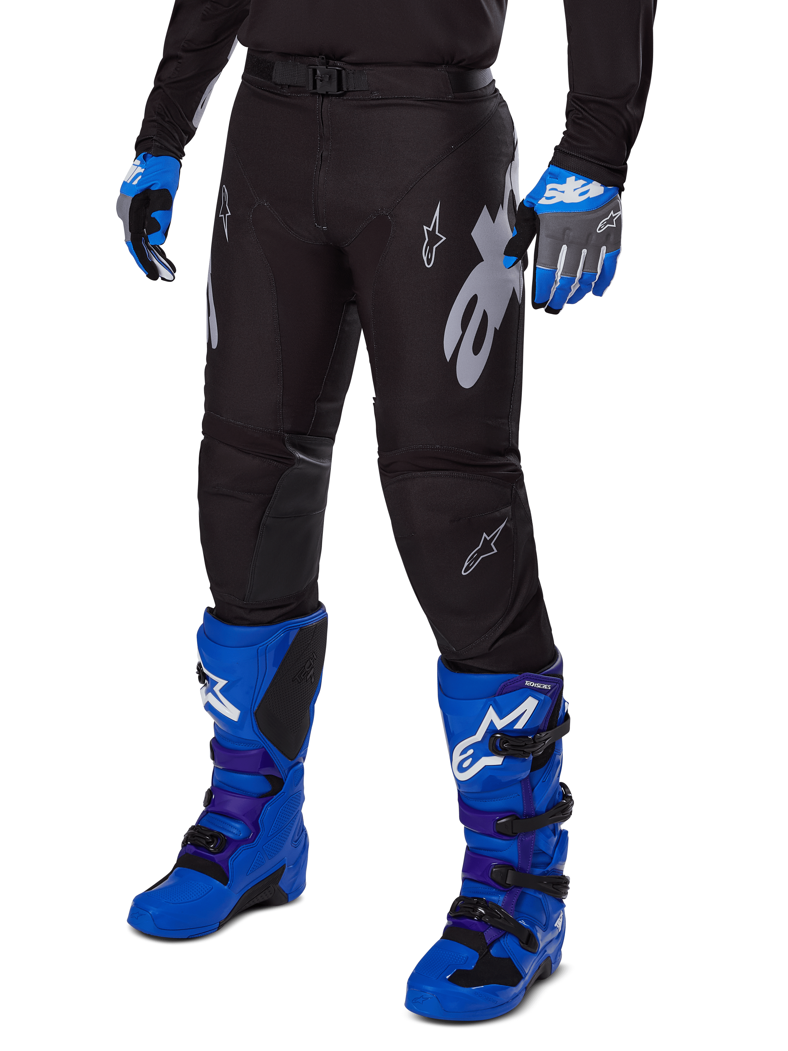 Alpinestars 2025 Racer Graphite Pants, czarne spodnie motocrossowe z białymi i szarymi grafikami, noszone z jasnoniebieskimi butami motocrossowymi i pasującymi niebieskimi rękawicami, wytrzymała tkanina techniczna do jazdy terenowej