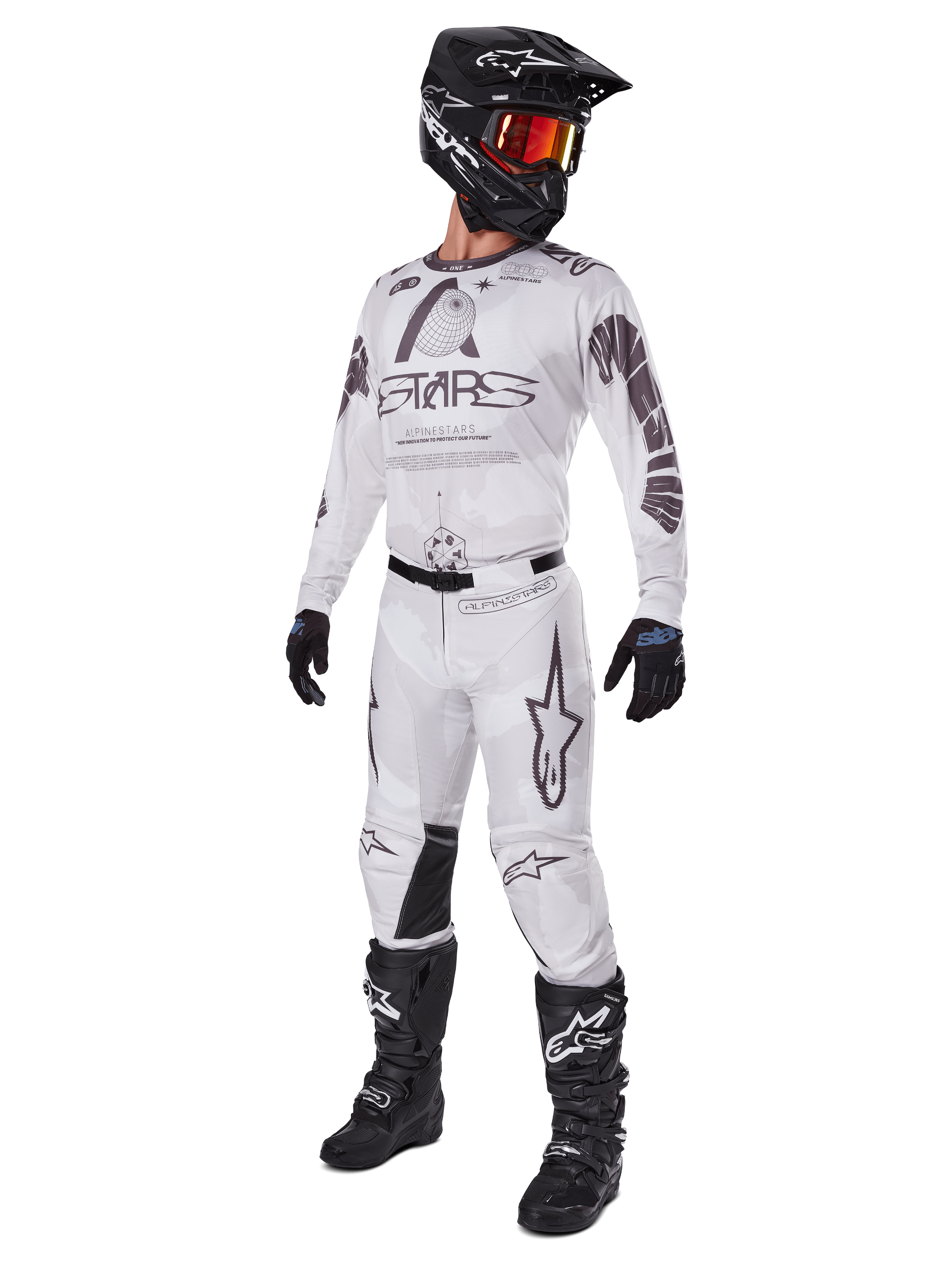 Alpinestars 2025 Racer Hollow Pants, spodnie motocrossowe, kolor Light Camo Brown, przedstawione jako część kompletnego zestawu wyścigowego z białą koszulką, czarnym kaskiem i czarnymi butami, z wzmocnionymi czarnymi panelami na kolanach i subtelnym wzorem kamuflażu.