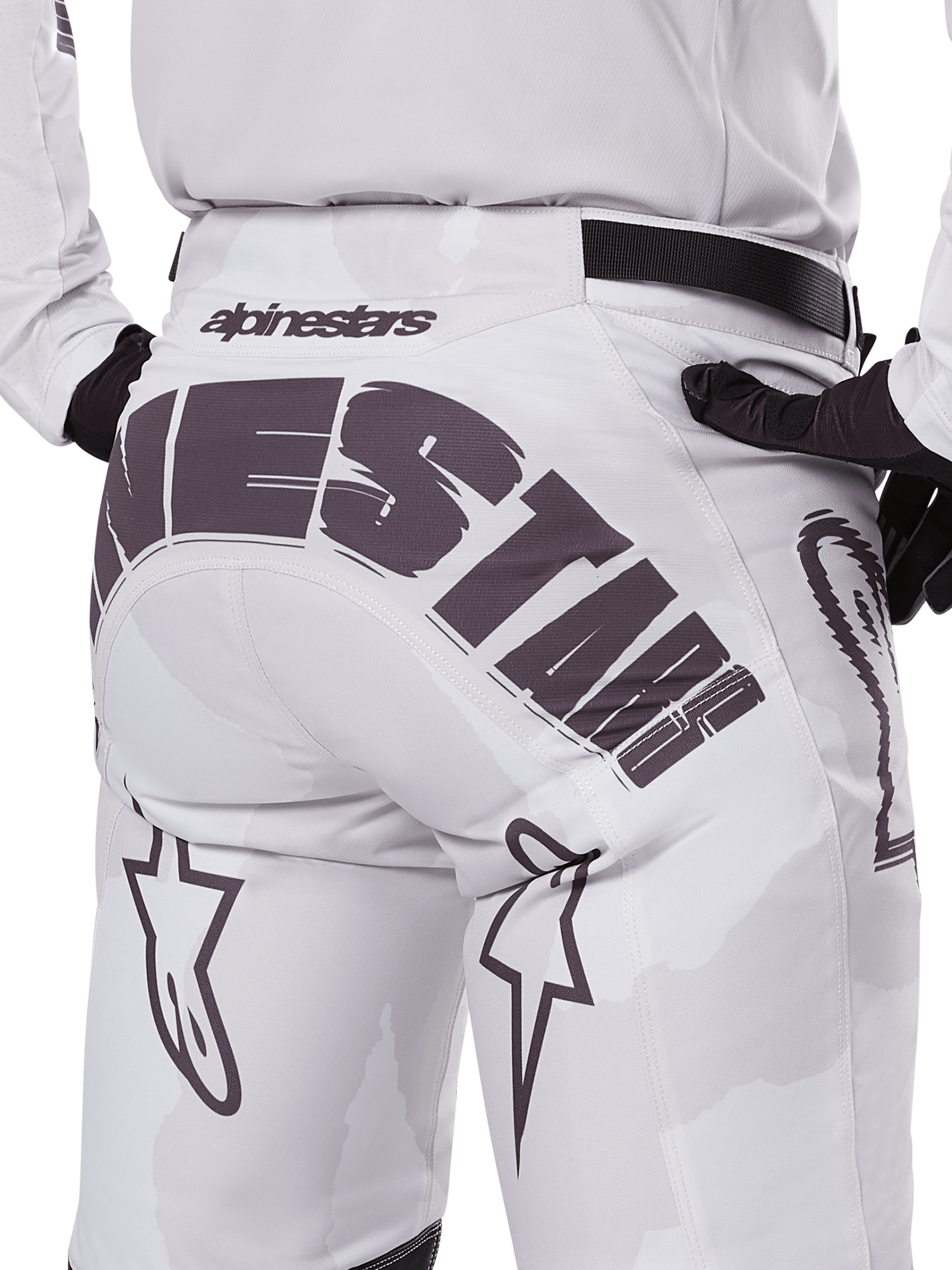 Widok z tyłu spodni Alpinestars 2025 Racer Hollow, spodnie motocrossowe, białe i jasny kamuflaż, z wyraźnym czarnym logo Alpinestars na siedzeniu, noszone z pasującą koszulką i czarnymi rękawicami