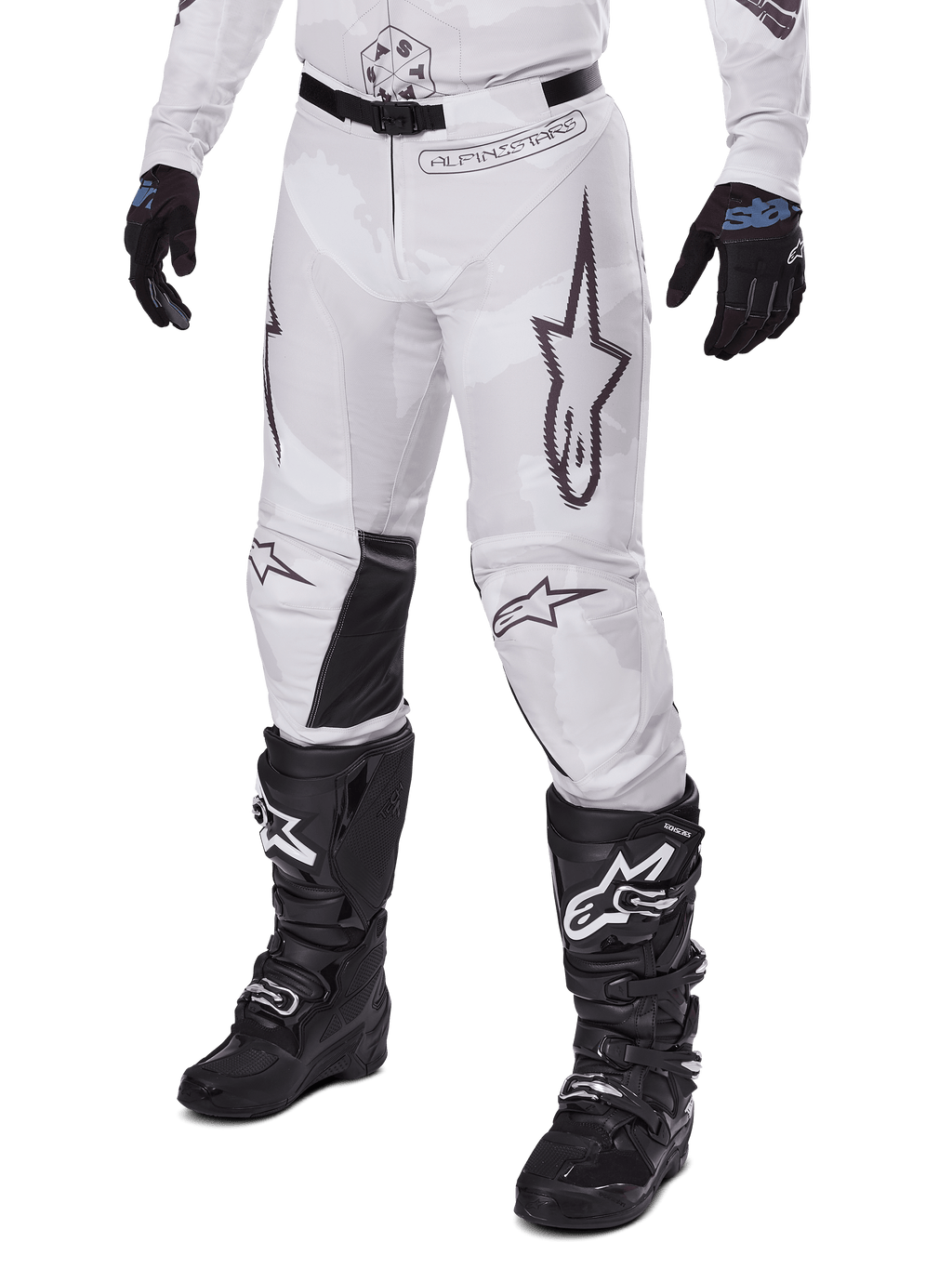 Alpinestars Racer Hollow Pants 2025, spodnie motocrossowe, biało-szary kamuflaż, z dużymi czarnymi konturowymi logo gwiazdy i czarnymi skórzanymi panelami po wewnętrznej stronie kolan, noszone z czarnymi butami i rękawicami motocrossowymi, wytrzymała konstrukcja do wyścigów terenowych.