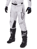 Alpinestars Racer Hollow Pants 2025, spodnie motocrossowe, biało-szary kamuflaż, z dużymi czarnymi konturowymi logo gwiazdy i czarnymi skórzanymi panelami po wewnętrznej stronie kolan, noszone z czarnymi butami i rękawicami motocrossowymi, wytrzymała konstrukcja do wyścigów terenowych.