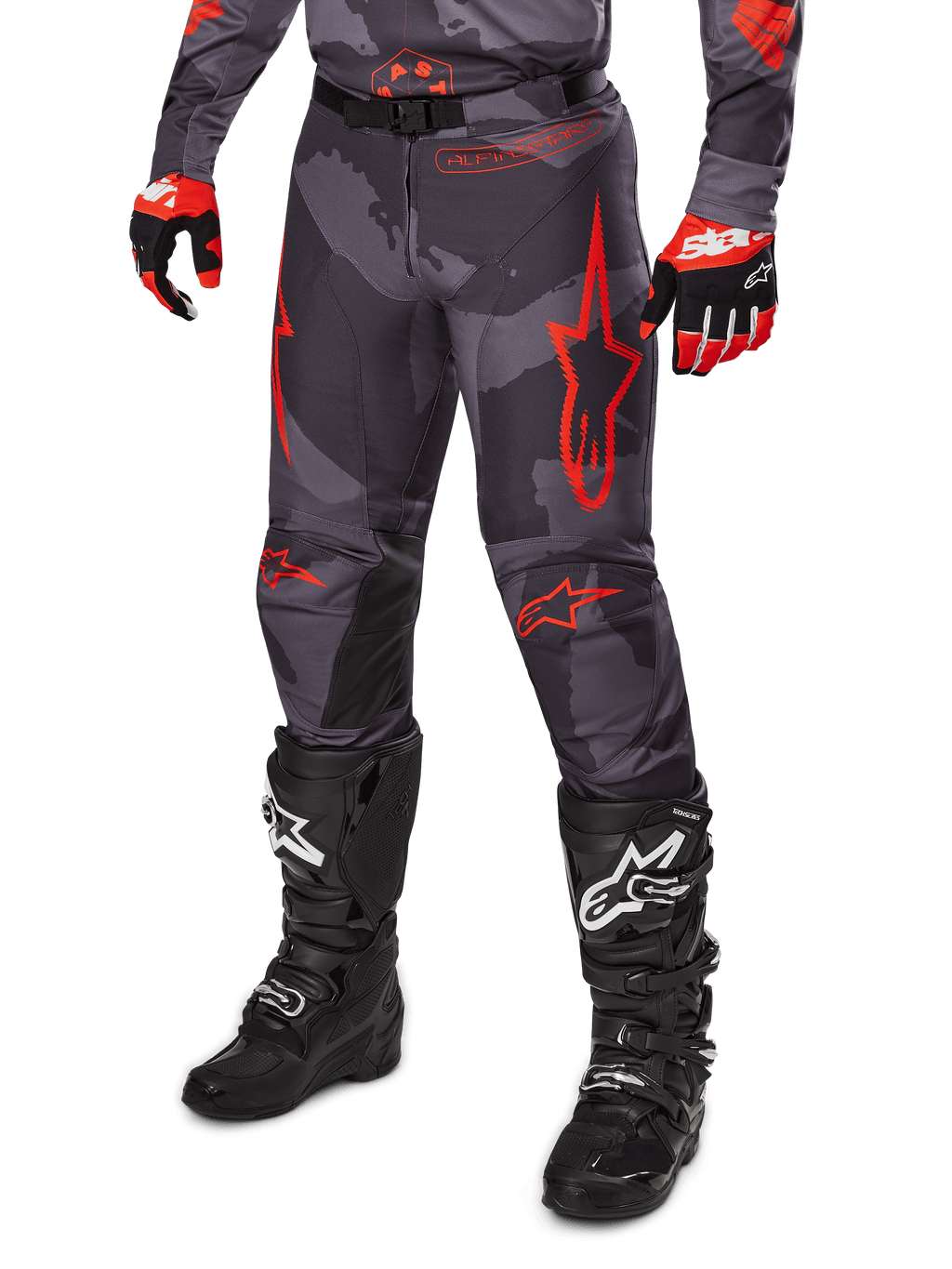 Alpinestars 2025 Racer Hollow Pants, spodnie motocrossowe, szare moro i czerwone, noszone z czarnymi butami i czerwonymi rękawicami, wyraziste czerwone logo w kształcie gwiazdy, wzór kamuflażu i wytrzymałe panele ochronne do jazdy terenowej