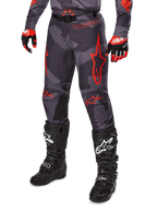 Alpinestars 2025 Racer Hollow Pants, spodnie motocrossowe, szare moro i czerwone, noszone z czarnymi butami i czerwonymi rękawicami, wyraziste czerwone logo w kształcie gwiazdy, wzór kamuflażu i wytrzymałe panele ochronne do jazdy terenowej