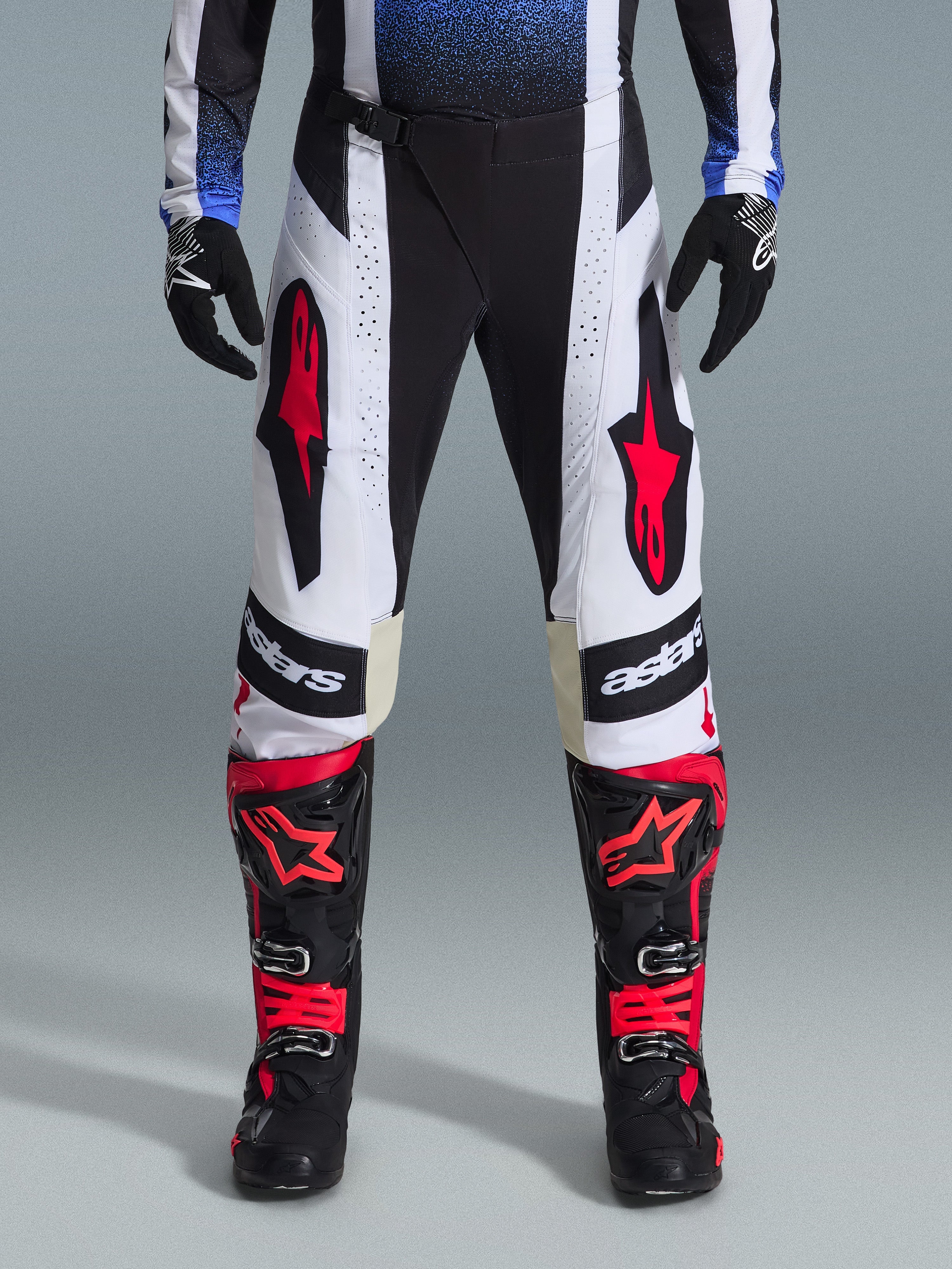 Alpinestars 2026 Techstar Knif Pants, spodnie motocrossowe, czarno-biało-czerwone, noszone z pasującymi czerwono-czarnymi butami i czarnymi rękawicami, z wyraźnymi czerwonymi logo gwiazdy na białych panelach i technicznymi perforowanymi detalami do wyścigów terenowych