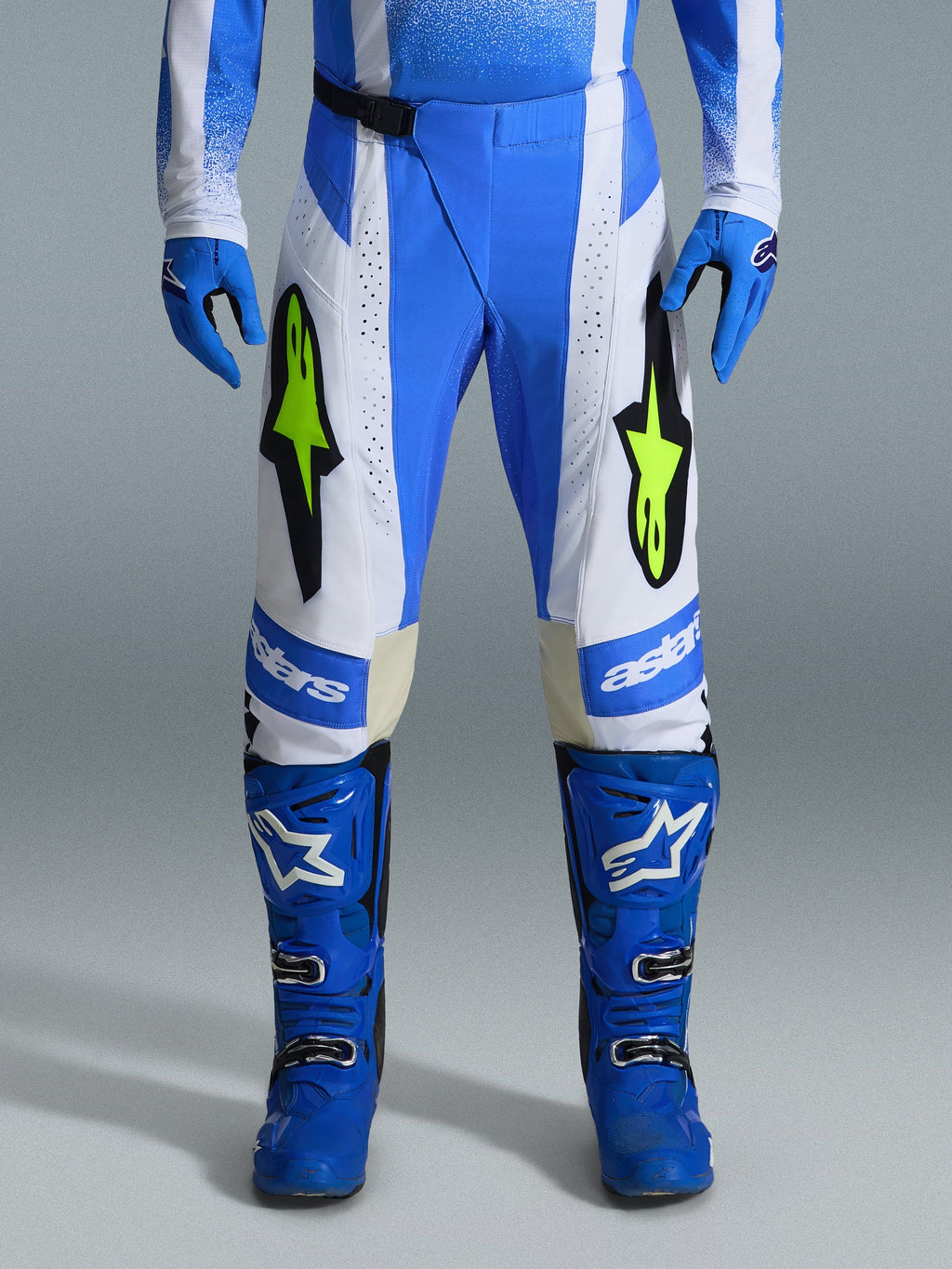 Alpinestars 2026 Techstar Knif Pants, spodnie motocrossowe, niebieskie UCLA, czarne i neonowe żółte, noszone z pasującymi niebieskimi rękawicami i butami, białe panele i wyraziste żółte logo fluo, ergonomiczny krój wyścigowy do jazdy w terenie